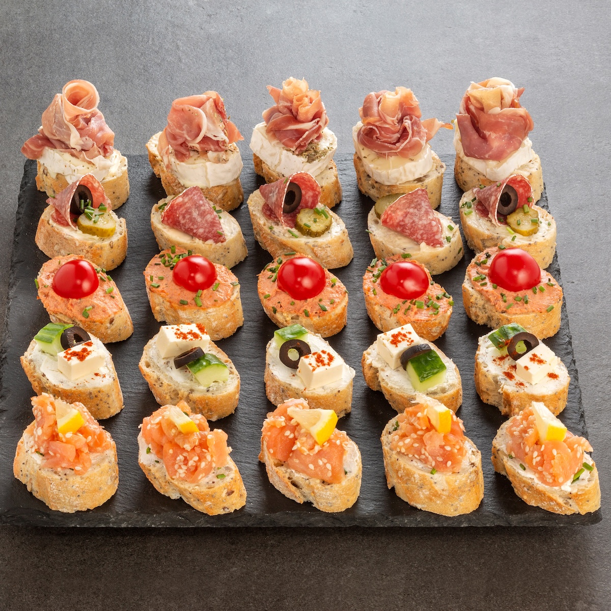 Vielfältiges Häppchen-Platte auf Schiefer: 20 Canapés mit Rohschinken, Salami, Räucherlachs, Frischkäse, Kirschtomaten und Oliven – Catering-Spezialität für Firmenevents in München