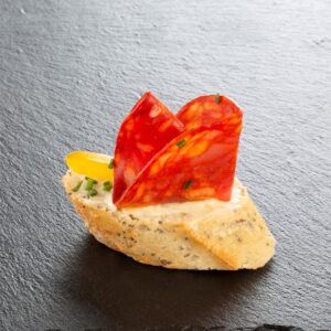 Chorizo-Häppchen auf Schiefer angerichtet: geröstetes Brot mit Frischkäse, Chorizo und gelber Paprika – Catering-Spezialität für Firmenevents in München