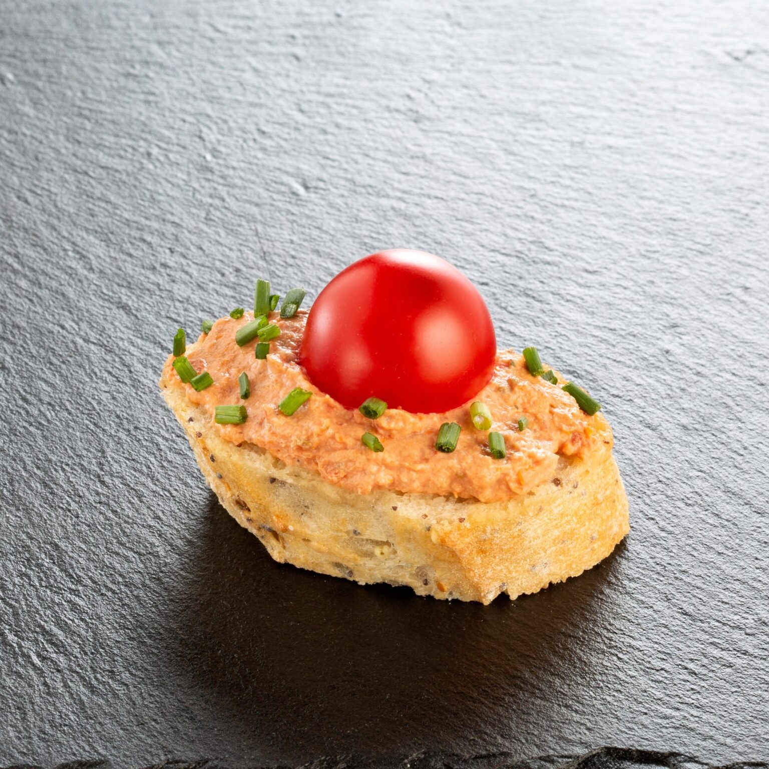 Provenzalisches Häppchen auf Schiefer angerichtet: Cracker mit würziger Mousse, Kirschtomate und Schnittlauch – Catering-Spezialität für Firmenevents in München