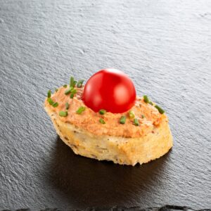 Provenzalisches Häppchen auf Schiefer angerichtet: Cracker mit würziger Mousse, Kirschtomate und Schnittlauch – Catering-Spezialität für Firmenevents in München