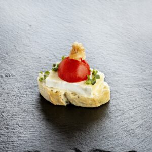 Elegantes Häppchen auf Schiefer angerichtet: geröstetes Brot mit frischem Käse, Kirschtomate und Schnittlauch – Catering-Spezialität für Firmenevents in München