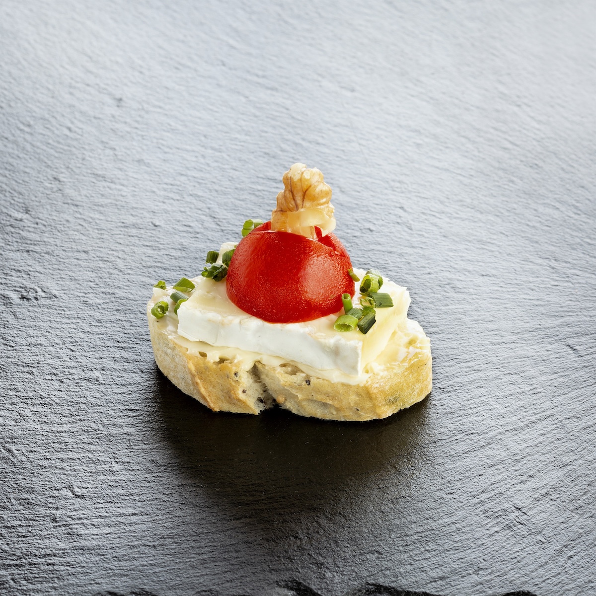 Elegantes Häppchen auf Schiefer angerichtet: geröstetes Brot mit frischem Käse, Kirschtomate und Schnittlauch – Catering-Spezialität für Firmenevents in München